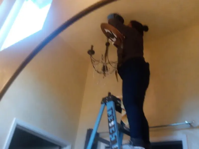 Electrician installing a chandelier in a Walton residence